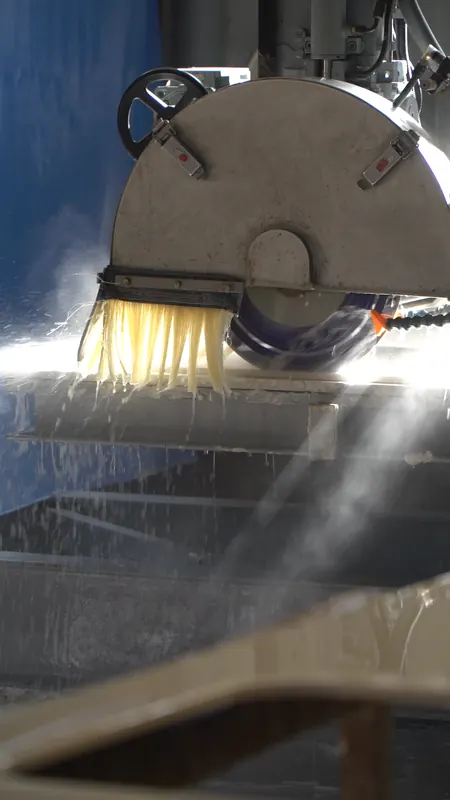 Un disco de corte atraviesa una placa de piedra entre una nube de agua pulverizada, en el taller.